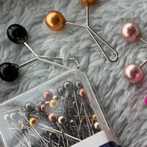 Box of dressmaker pins with pins spilling out on a textured surface